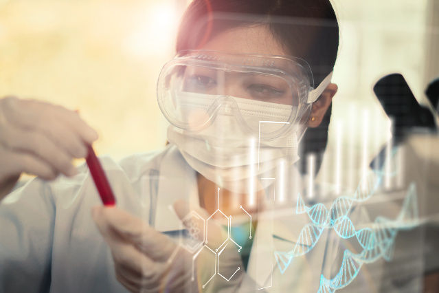 eine Frau mit Schutzbrille ist in einem Labor und hält ein Reagenzglas in der Hand (verweist auf: Medizinische Forschung - Neue Entwicklungen in der Forschung mit Gesundheitsdaten)